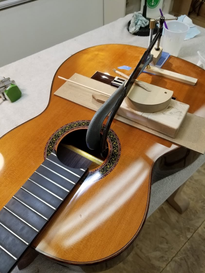 № 1061 on a workbench, a deep-throated clamp reaching through the soundhole to hold the repair